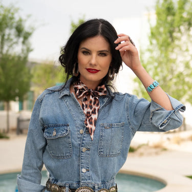Leopard Twilly by Fringe Scarves at 6Whiskey, six whisky, leopard print, animal print, fun, flirty, western, bold, edgy, cool, stylish, chic, western accessory, womens accessory, eye catching, modern western. Pair with maroon or burgundy for an aggie gameday look, game day style, Texas A&M outfit inspo, aggies game day accessory. Cream, black, brown leopard print. front view styled on woman tied in a bow with denim and silver and turquoise jewelry.