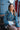 magnolia blouse at 6whiskey six whisky cleobella. A woman sits on a decorative metal bench in a small Texas town, wearing a blue floral long-sleeve blouse with gathered details and white high-rise shorts.