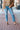 Hailey High-Rise Jeans at 6Whiskey six whisky. Women’s jeans department-a model wears light wash, high-rise straight-leg jeans with subtle knee distressing and a raw hem, styled with brown sandals, a patterned knit tank, and a tan utility jacket on a brick sidewalk.