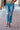 Hailey High-Rise Jeans at 6Whiskey six whisky. Women’s jeans department-a model wears light wash, high-rise straight-leg jeans with subtle knee distressing and a raw hem, styled with brown sandals, a patterned knit tank, and a tan utility jacket on a brick sidewalk.