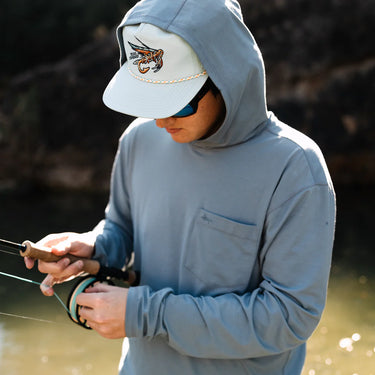 Man wearing Texas Standard Brazos Hoodie in Bayou Blue while fly fishing, showcasing UPF 50+ sun protection, moisture-wicking performance, and breathable stretch fabric – available at 6Whiskey, Texas lifestyle clothing store