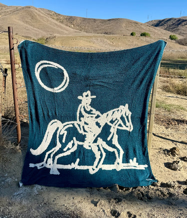 Lone Rider Blanket in teal at 6Whiskey, six whisky, blue, soft blanket, cozy, warm, comfortable, bed, couch, patio, bench, gift idea, western home decor, unique throw blanket, square blanket, large, handrawn design, country, ranch, front view.