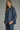 Denim darling blouse at 6whiskey, six whisky, woman wearing a blue denim blouse with jeans, ideal for fall game day or tailgate looks at texas a&m, aggies, SEC, gameday outift inspo, ruffle detail blouse with buttons and self tie, elasticated gathered long sleeve blouse, front and side view, football game outfit, watch party look, game day to weekday look. Pair with maroon or burgundy accessories and sneakers, sandals, or boots. Texas A&M casual chic aggie style.