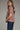 Gridiron gingham blouse at 6whiskey, six whisky, woman wearing a burgundy maroon gingham print blouse with jeans, ideal for fall game day or tailgate looks at texas a&m, aggies, SEC, gameday outift inspo, elasticated gathered mid length sleeve blouse, side view, football game outfit, watch party look, game day to everyday look. Pair with black, white, or blue jean denim or aggie accessories and sneakers, sandals, or boots. Texas A&M aggie style. Casual chic aggie style.