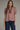 Gridiron gingham blouse at 6whiskey, six whisky, woman wearing a burgundy maroon gingham print blouse with jeans, ideal for fall game day or tailgate looks at texas a&m, aggies, SEC, gameday outift inspo, ruffle detail blouse, elasticated gathered mid length sleeve blouse, front view, football game outfit, watch party look, game day to everyday look. Pair with black, white, or blue jean denim or aggie accessories and sneakers, sandals, or boots. Texas A&M aggie style. Casual chic aggie style.