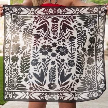 Senorita black and white bandana by Fringe Scarves at 6Whiskey, six whisky, floral theme, white, black, pair with burgundy or maroon, square, soft, comfortable, breathable, year-round, must-have, eye-catching, classic western, timeless, elevated, front view. Scarf with floral & geometric design held by a person in a rustic setting. Texas A&M gameday, game day, A&M, Aggie style, western aggie style for gamedays, football gameday style SEC, wear to Kyle field or tailgates.