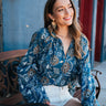 magnolia blouse at 6whiskey six whisky cleobella. A woman sits on a decorative metal bench in a small Texas town, wearing a blue floral long-sleeve blouse with gathered details and white high-rise shorts.