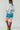 6Whiskey High Noon distressed denim shorts for women, featuring a mid-thigh length, raw hem, and vintage-inspired wash, styled with a white long-sleeve top