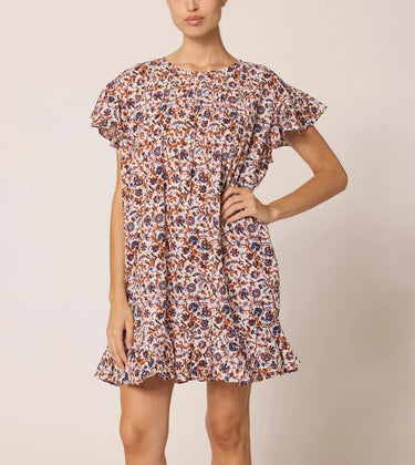 Aurora Mini Dress at 6Whiskey six whisky Cleobella. A woman wearing a short, flutter-sleeve mini dress with a high neckline, removable waist sash, and an allover floral print in earthy tones; the dress features a ruffled hem and side pockets, styled with brown ankle-strap sandals.