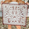 Down south bandana at 6whiskey, six whisky, Texas A&M maroon burgundy western icon graphic, maroon and white, soft, lightweight, breathable, comfortable, accessory, scarf, bandana, gameday, tailgating, football, SEC, western, casual. Front view. Woman wearing white dress holding bandana. Tie on neck, wrist, beltloops, or on purse. Aggie style and gameday outfit inspo. Horseshoe, boots, bucking horse and cowboy and cactus.
