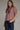 Gridiron gingham blouse at 6whiskey, six whisky, woman wearing a burgundy maroon gingham print blouse with jeans, ideal for fall game day or tailgate looks at texas a&m, aggies, SEC, gameday outift inspo, ruffle detail blouse, elasticated gathered mid length sleeve blouse, front/ side view, football game outfit, watch party look, game day to everyday look. Pair with black, white, or blue jean denim or aggie accessories and sneakers, sandals, or boots. Texas A&M aggie style. Casual chic aggie style. 