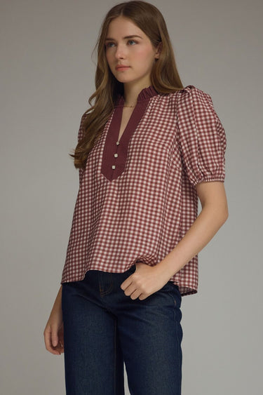 Gridiron gingham blouse at 6whiskey, six whisky, woman wearing a burgundy maroon gingham print blouse with jeans, ideal for fall game day or tailgate looks at texas a&m, aggies, SEC, gameday outift inspo, ruffle detail blouse, elasticated gathered mid length sleeve blouse, front/ side view, football game outfit, watch party look, game day to everyday look. Pair with black, white, or blue jean denim or aggie accessories and sneakers, sandals, or boots. Texas A&M aggie style. Casual chic aggie style. 